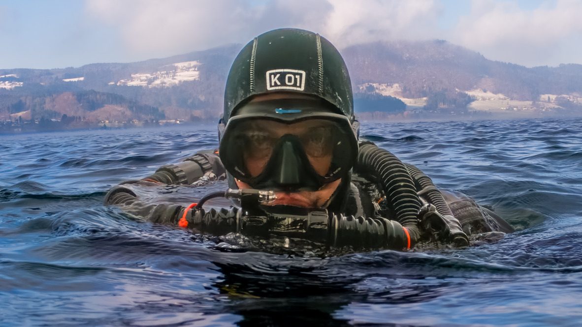 Christian Feichtinger an der Oberfläche des Attersees, im Hintergrund verschneite Berge