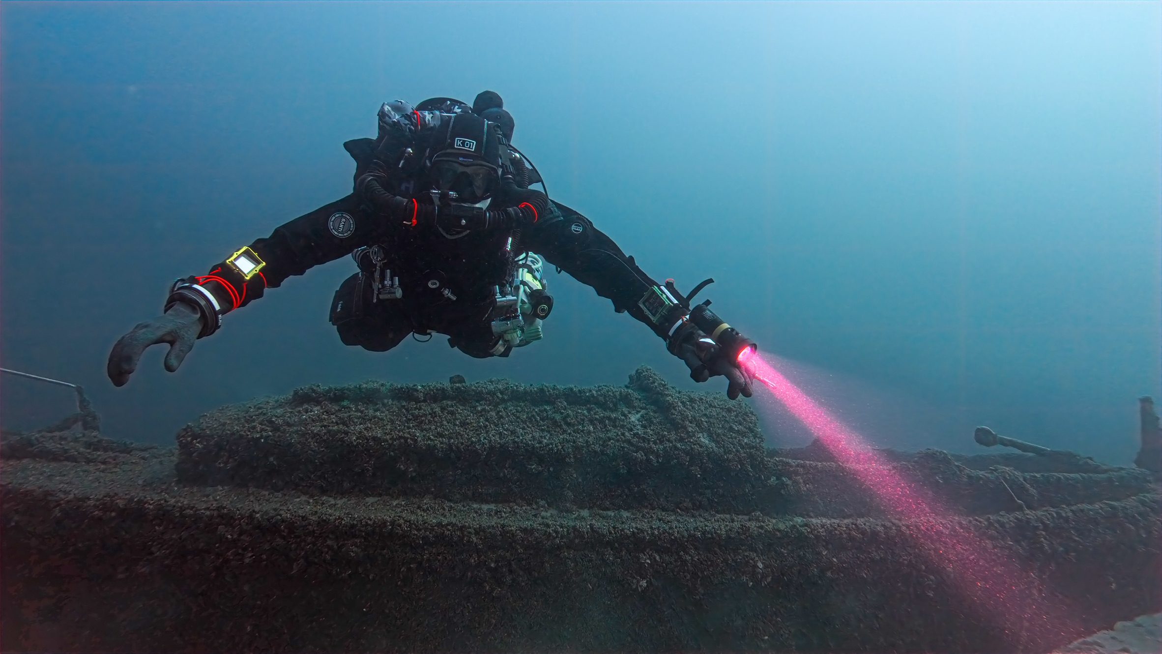Taucher mit Lampe über einem bewachsenen Wrack im Attersee
